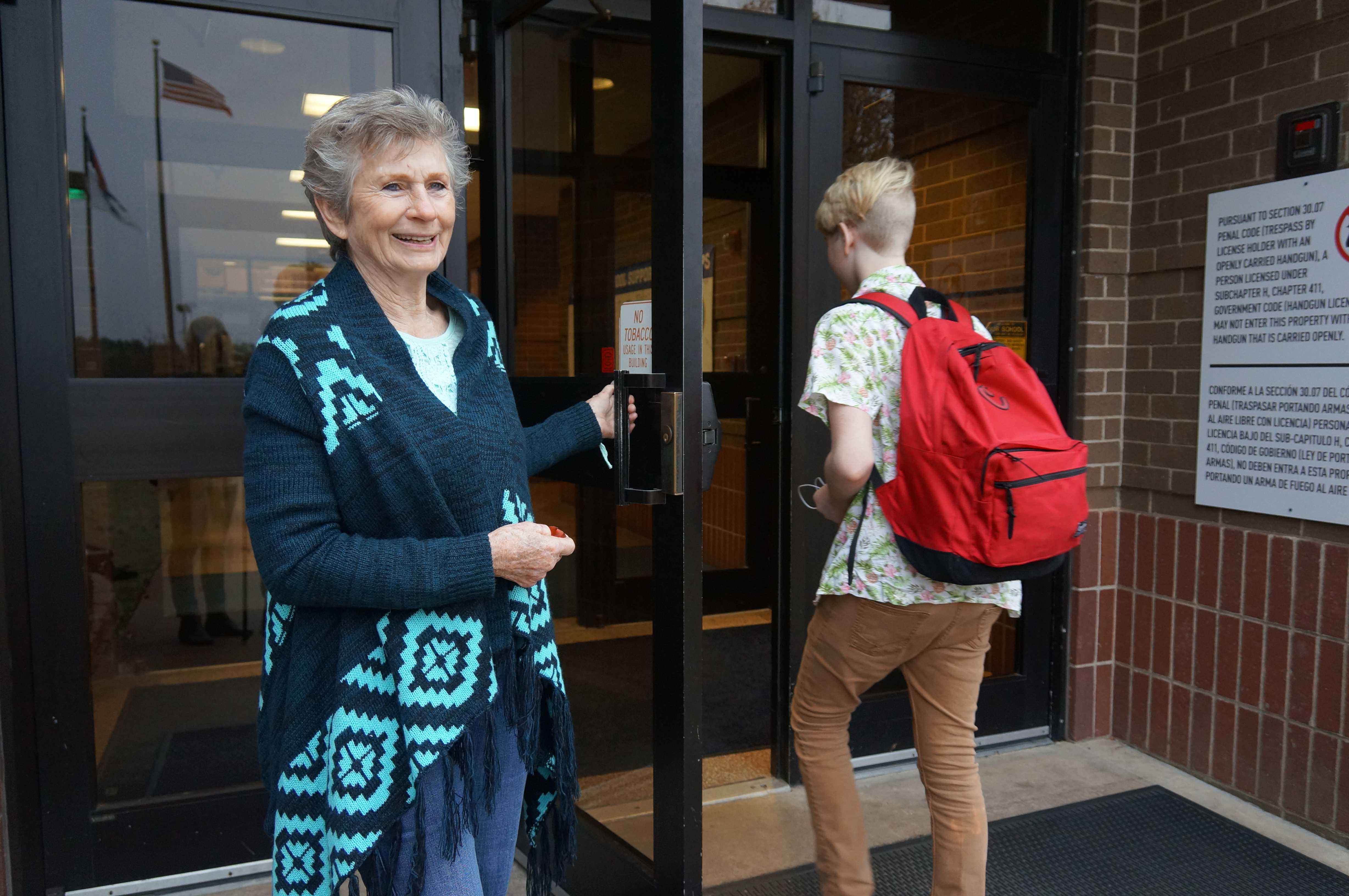 Volunteer Betty Hicks holds the door open for a student.