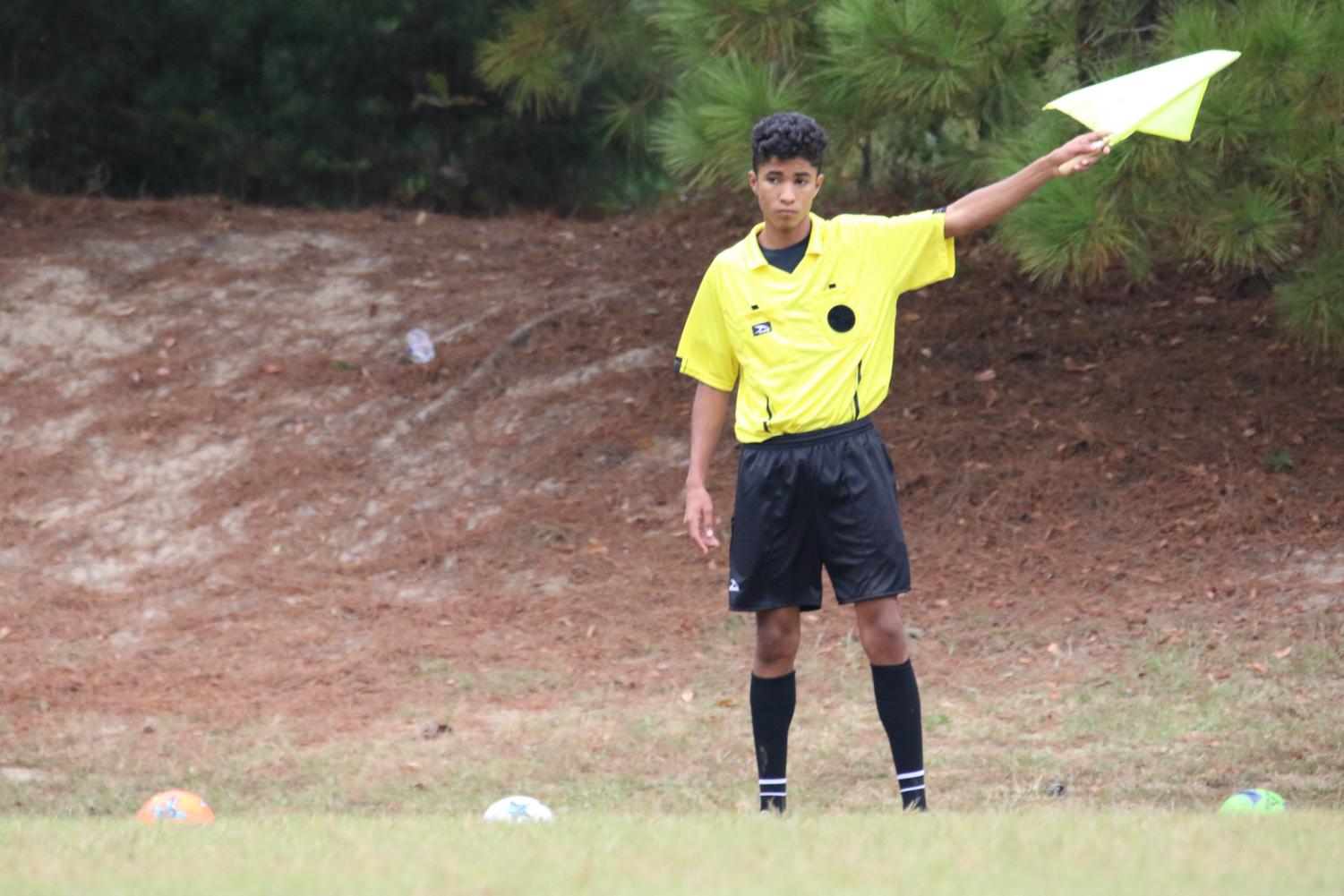Sophomore soccer referee Salomao Saboia raises his flag to make a call. He is from Brazil, the soccer country of the world, and he has played soccer for most of his life. This is his first season refereeing.