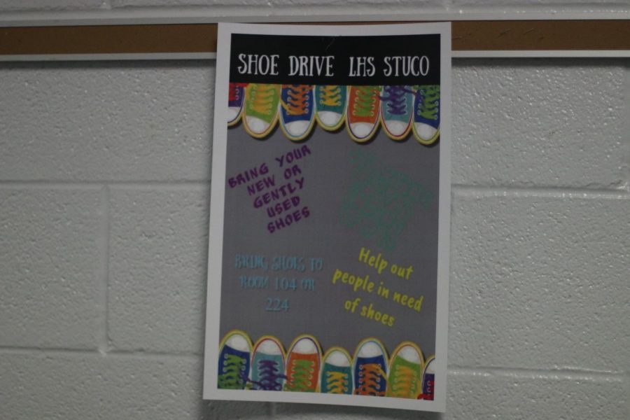 The poster hangs in the school hallway. This is used to advertise the fact that there is a shoe drive.