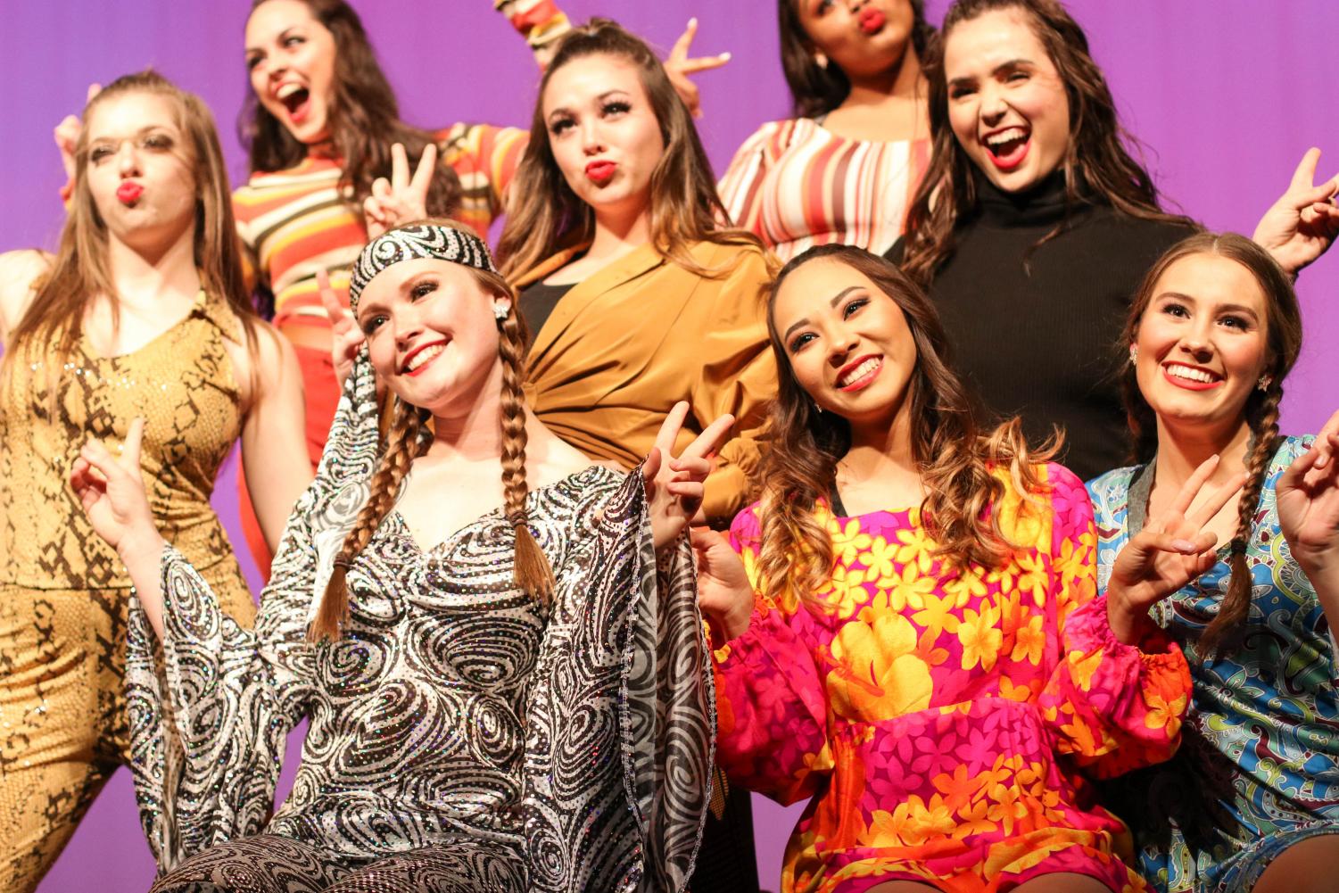Seniors Maryann Castaneda and Kayley Kraig along with junior Autumn Brown along with other drill team members hold up peace signs to end their dance routine. They performed in attire from the 1960s-1970s era. 