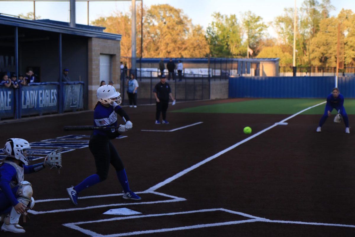 A softball player swings for the ball at a varsity game.