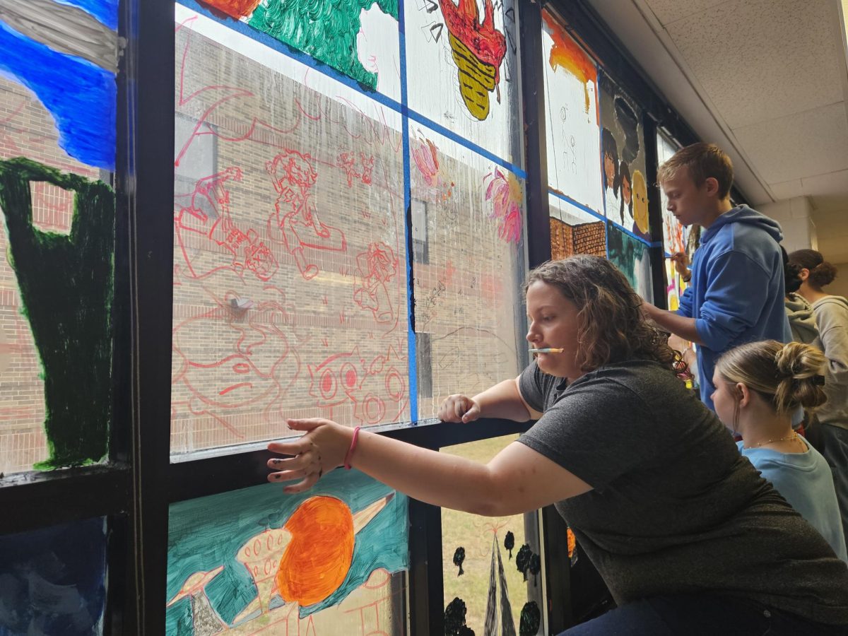 Senior Tevi Lane climbs onto a stool to paint the art classroom window. She sketched her design with a dry erase marker prior to painting.