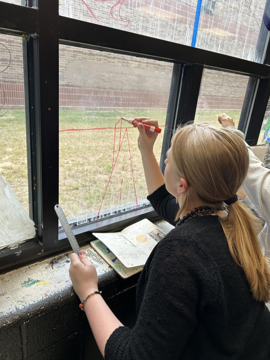 Junior Laila Lindsey sketches her design onto the art classroom window. She used perspective to create the theme of “bright future.”